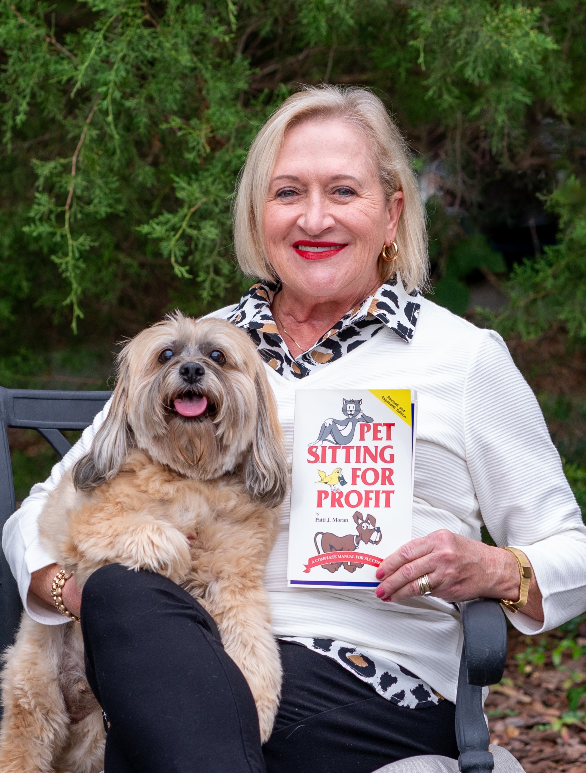 PSI Founder and CEO Patti Moran sits on a bench holding a dog and a book.