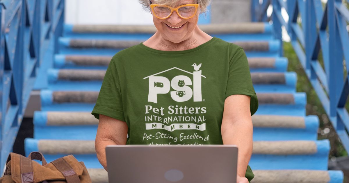 Pet sitter wearing a PSI member t-shirt is sitting on outdoor steps working on her laptop.