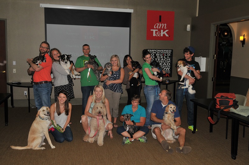 Several employees pose for a photo with their dogs indoors at a Take Your Dog To Work Day event.